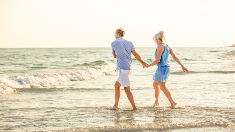 boomer couple holding hands and walking in the Gulf waves