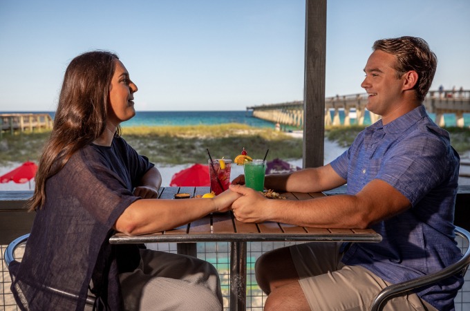 couple holds hands while enjoy drinks on Windjammers deck with beach view